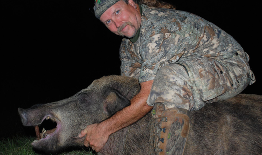 Glenn Guess in camouflage clothing, poses on top of a wild boar he has hunted.