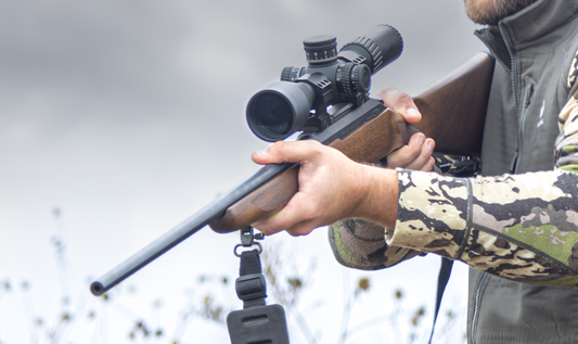 A close-up image of a hunter holding a bolt-action rifle with a wooden stock and a large Sightmark Presidio riflescope attached.