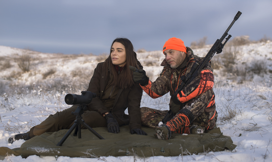 Two hunters, a man and woman, in a snowy landscape, preparing for a hunt.