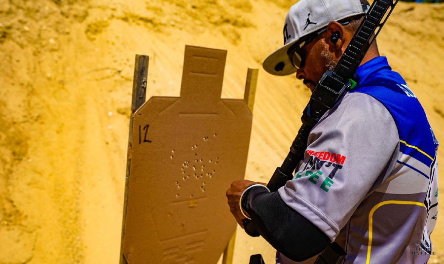 Chris Spence, a competitive shooter examines a paper target with multiple bullet holes during a shooting match.