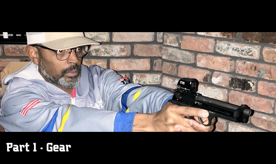 A man wearing glasses and a baseball cap is holding a handgun equipped with a red dot sight.